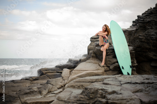 Sporty girl in the multi colored swimsuit sitting near the surf on the rock