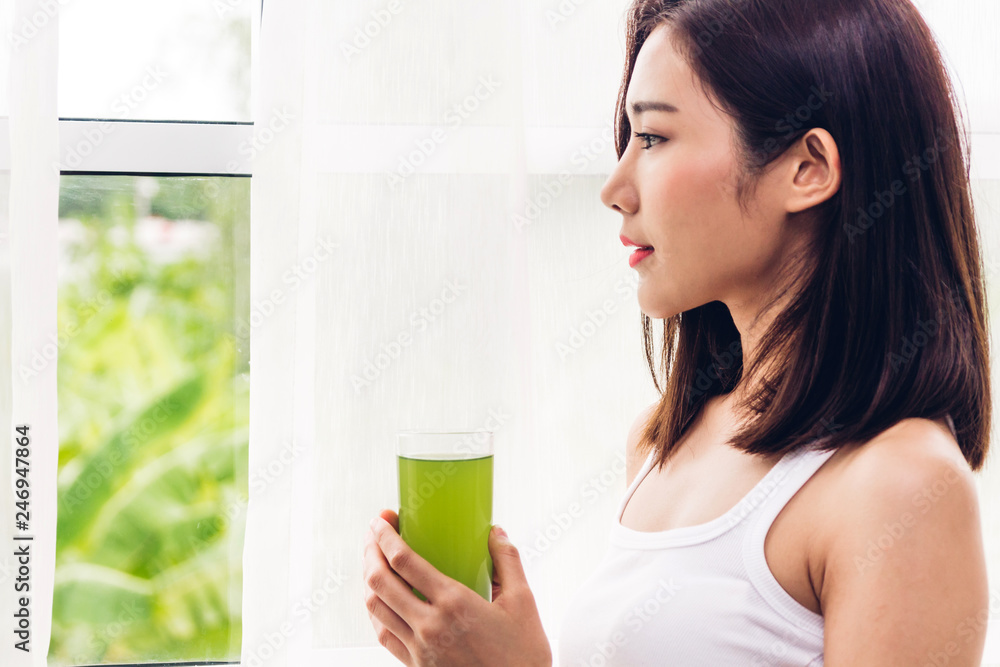 Woman enjoy healthy drinking green detox vegetable juice near window curtains in the living room at home.dieting concept.healthy lifestyle Woman enjoy healthy drinking green detox vegetable juice near window curtains in the living room at home.dieting concept.healthy lifestyle