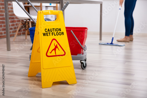Cleaner Standing With Mop And Caution Wet Floor Sign