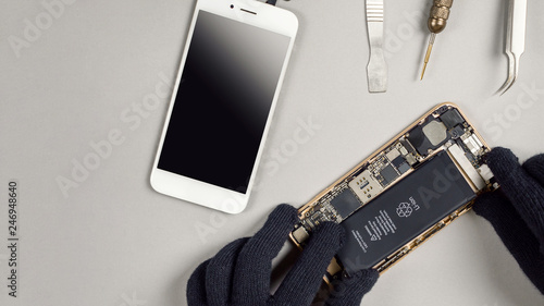 Technician or engineer disassembling components broken smartphone for repair or replace new smartphone battery on desk with copy space