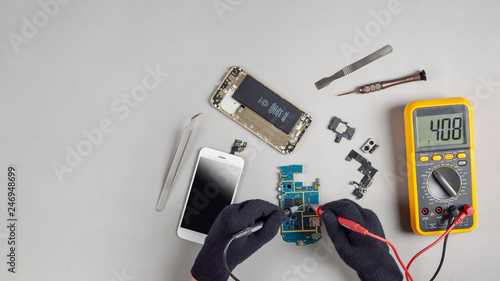 Technician or engineer using digital multimeter to electric current measurement on smartphone logic board for diagnosis broken smartphone with copy space photo