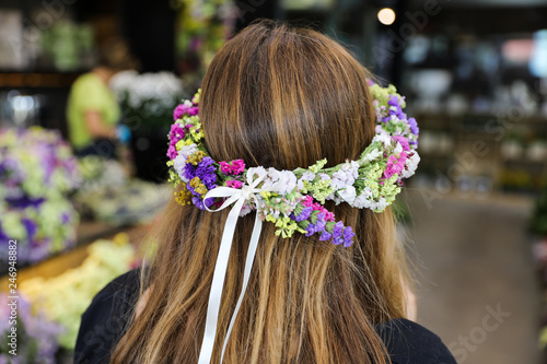 A beautiful wreath of of limonium sinuatum or statice salem flowers in blue, lilac, violet, pink, white, yellow colors on the head of a girl with long brown hair.