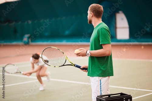 Male Coach watching as his female student hits the ball on indoor playground