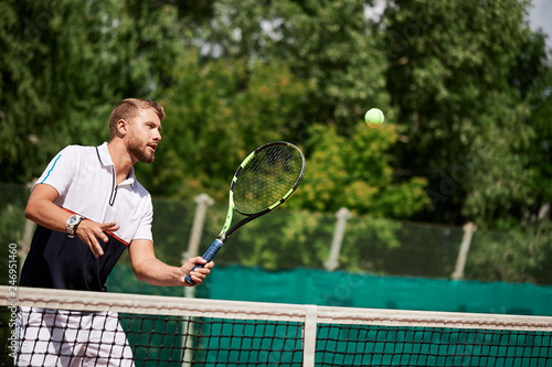 Concentrated blonde bearded male tennis player is ready to make a strong serve onoutdoor summer court