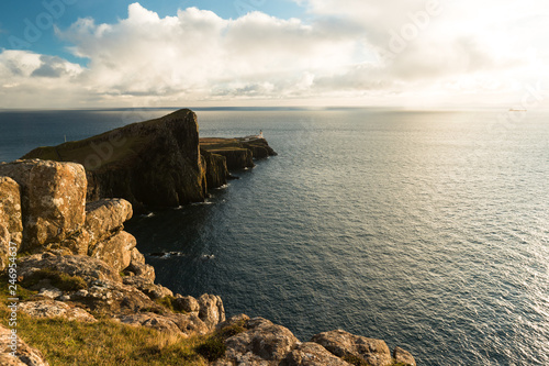 Sunset at Neist Point Lighthouse with rocky shore, dramatic sky and sun bursting through clouds before sunset (Isle of Skye, Scotland, Europe)