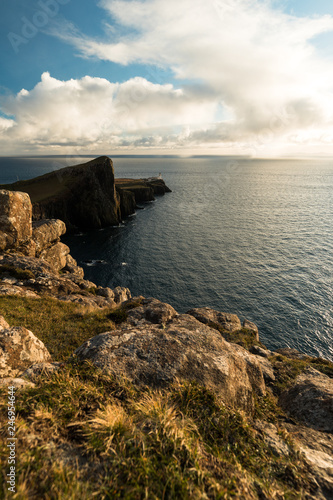 Sunset at Neist Point Lighthouse with rocky shore, dramatic sky and sun bursting through clouds before sunset (Isle of Skye, Scotland, Europe)