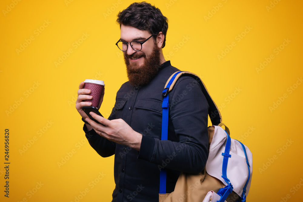 Smiling bearded man walking and using smartphone. Handsome guy standing and holding drink. Smiling bearded man walking and using smartphone. Handsome guy standing and holding drink.
