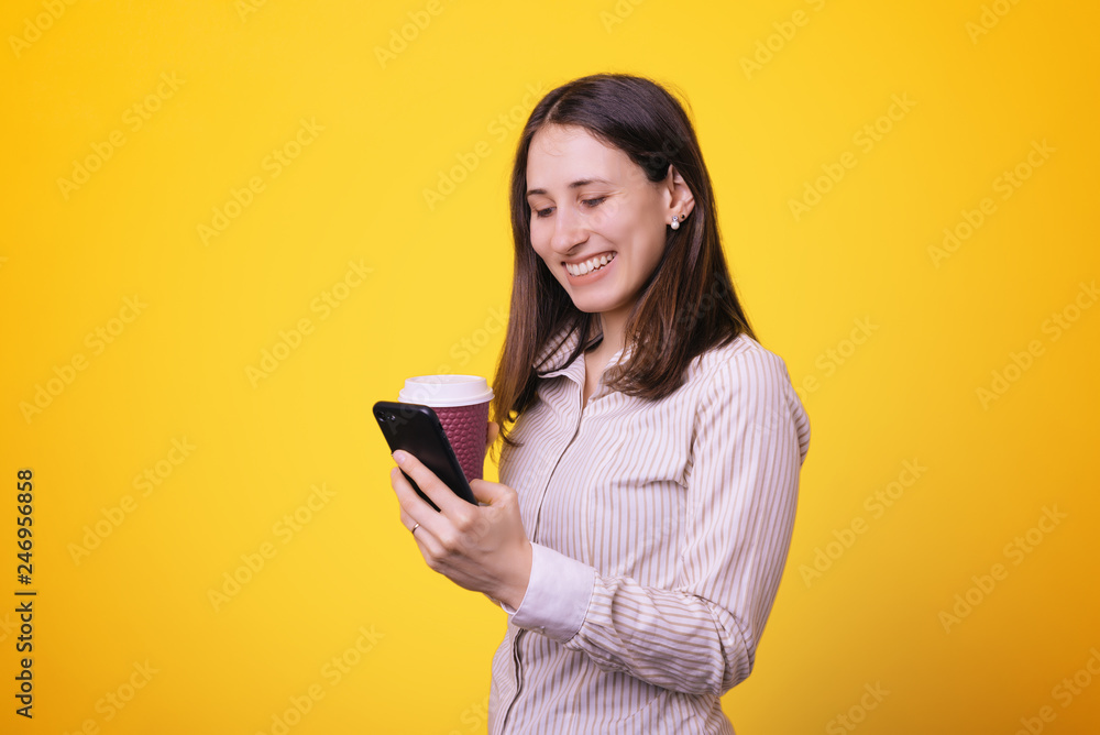 Pretty ypung woman using smartphone and drinking coffee, over colorful yellow background Pretty ypung woman using smartphone and drinking coffee, over colorful yellow background