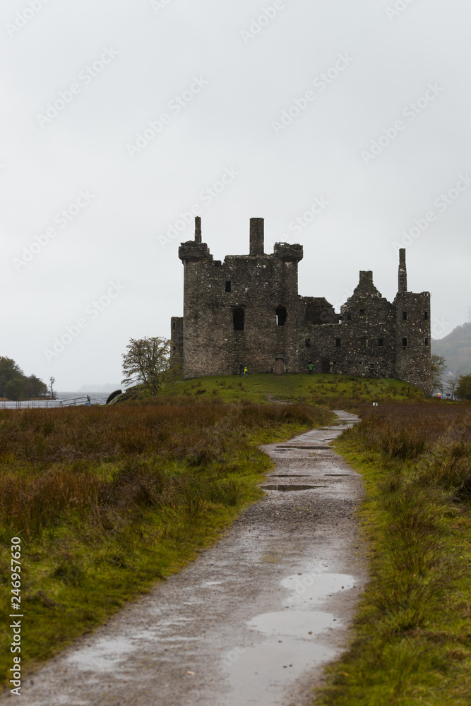 Close-up of the ruins of Kilchurn Castle near Loch Lomond during a rainy autumn day with path to castle (Scotland, United Kingdom, Europe)