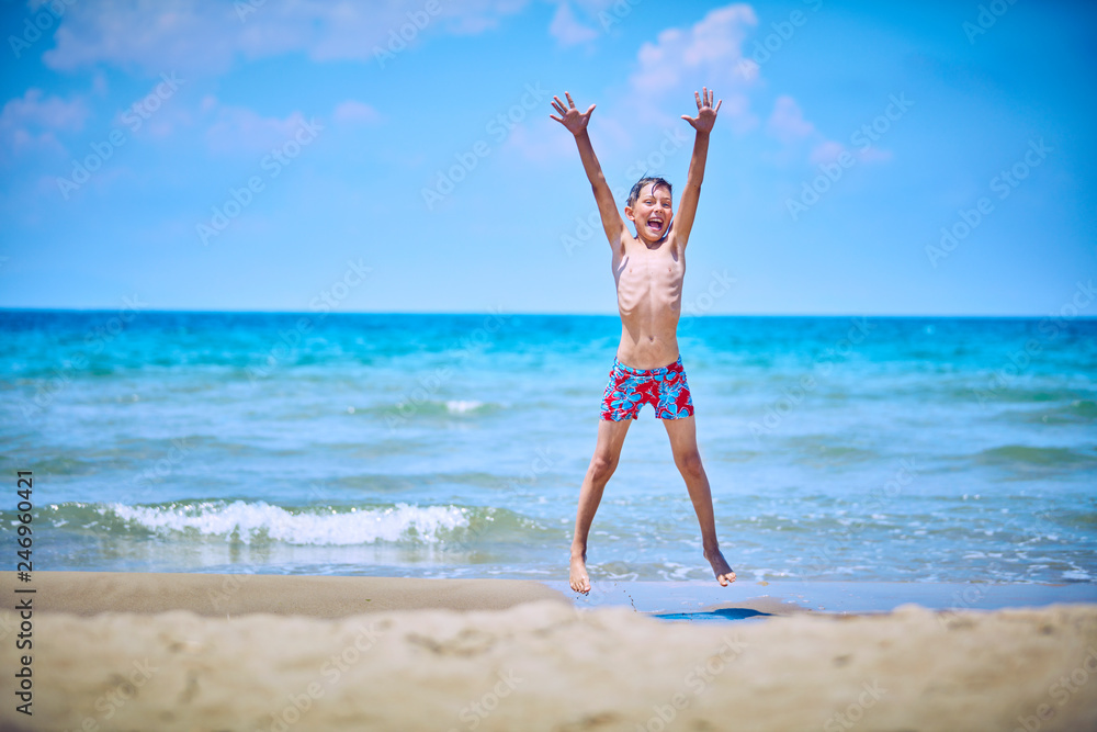 Adorable happy boy jumping and playing on the beach.