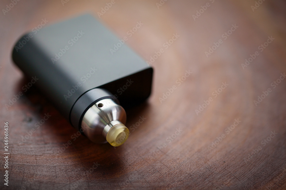 high end rebuildable dripping atomizer with black regulated box mods on wood texture background, vaping device, selective focus with shallow depth of field high end rebuildable dripping atomizer with black regulated box mods on wood texture background, vaping device, selective focus with shallow depth of field
