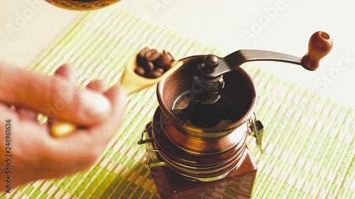 Male hands pouring coffee beans into a hand mill for grinding.