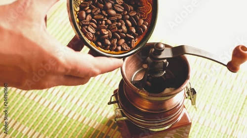 Male hands pouring coffee beans into a hand mill for grinding.