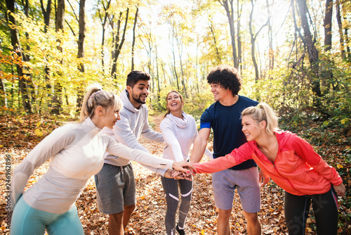 Happy group of runners smiling and stacking hands while standing in woods in autumn.