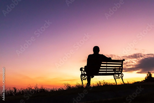 Silhouette of woman sitting alone on the bench against twilight sky over a mountain. 