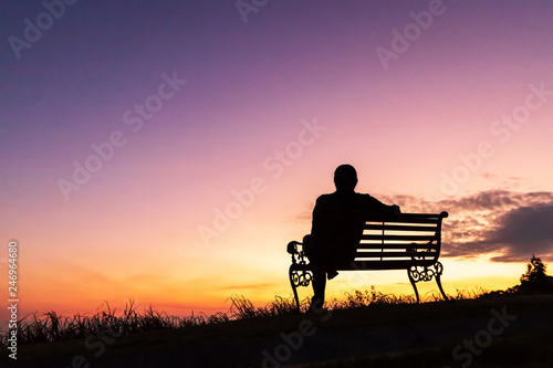 Fotografie Silhouette of woman sitting alone on the bench against twilight sky over a mountain