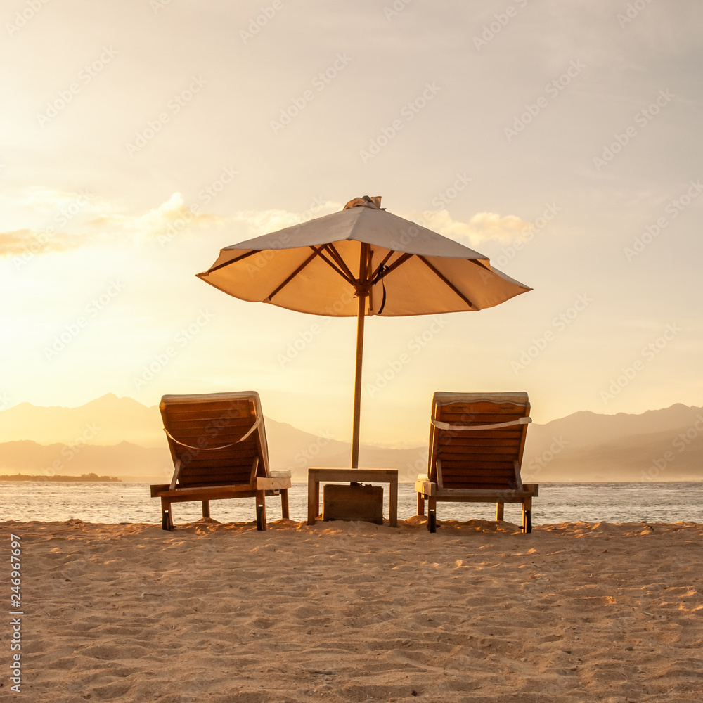 Squared image of two beautiful chairs and umbrella parasol on a paradise sandy beach at sunset. 