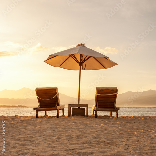 Squared image of two beautiful chairs and umbrella parasol on a paradise sandy beach at sunset.  © pcruciatti