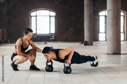 strong motivated man doing plank with kettlebells during workout at gym while his girlfriend looking at him. hobby, interest, motivation