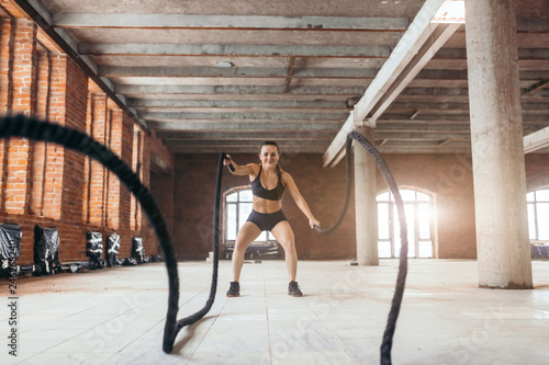 cheerful girl training with battle rope at cross fit gym. full length photo. hobby, lifestyle, fitness