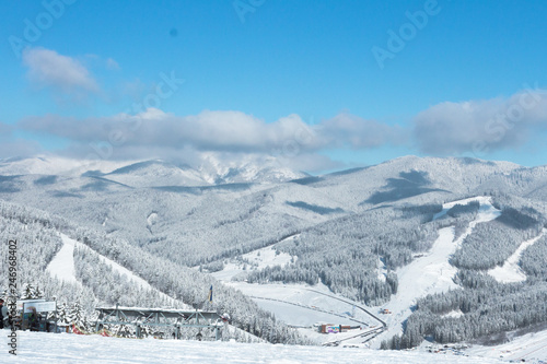 View of the Ukrainian Carpathians. Ski resort Bukovel. Snowy mountains. Spruce forest. Ski slopes for skiers and snowboarders. Winter sport. Chalet in a mountain village. Sunny frosty weather.
