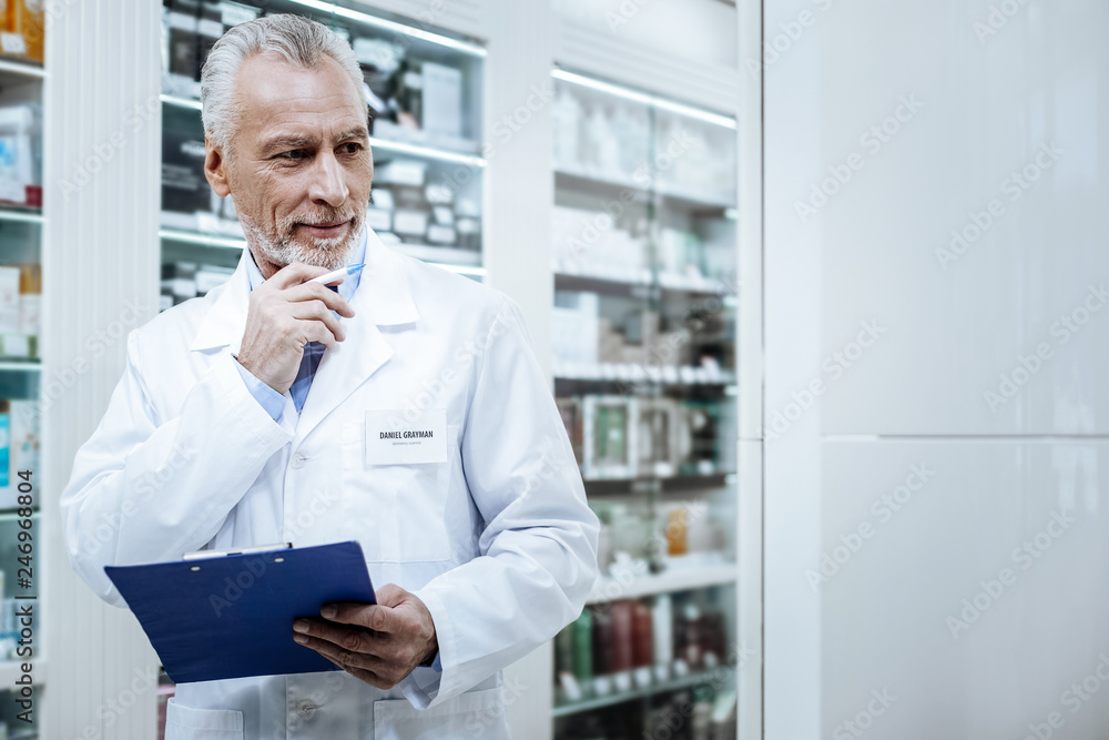 Grey-haired bearded pharmacist in a blue shirt comparing medicines