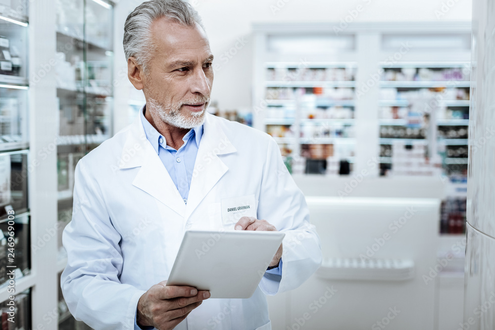 Grey-haired positive pharmacist in a white coat making a revision
