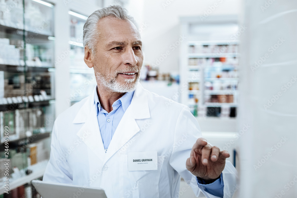 Director of a drugstore in a white coat examining the show case in a drugstore
