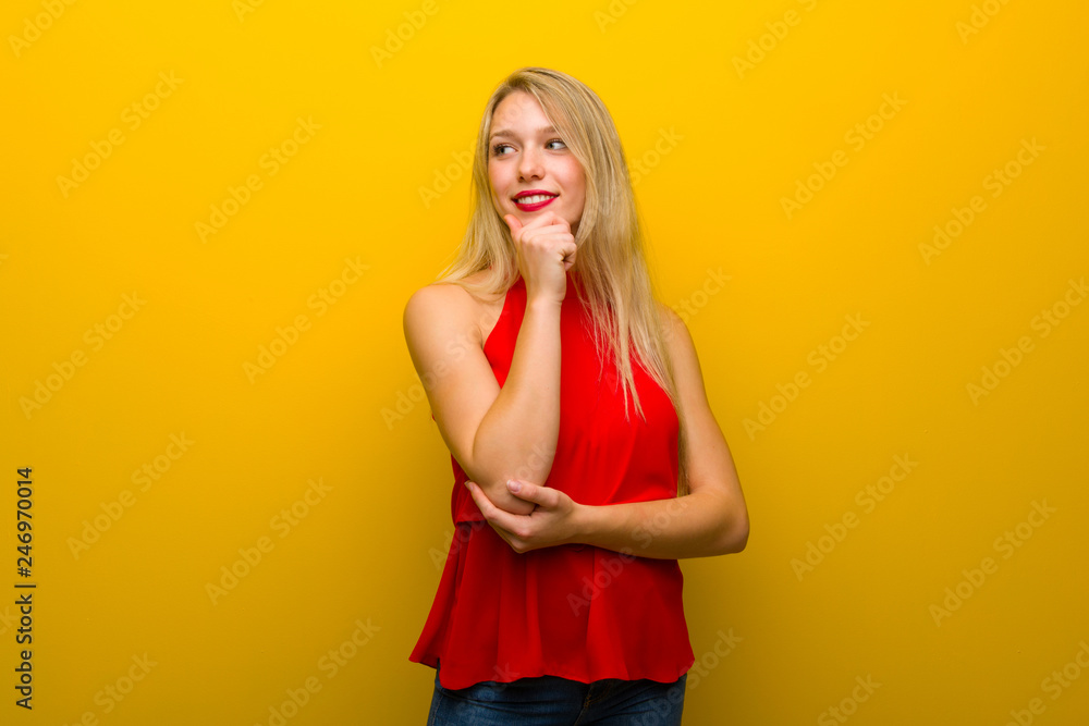 Young girl with red dress over yellow wall looking to the side with the hand on the chin Young girl with red dress over yellow wall looking to the side with the hand on the chin
