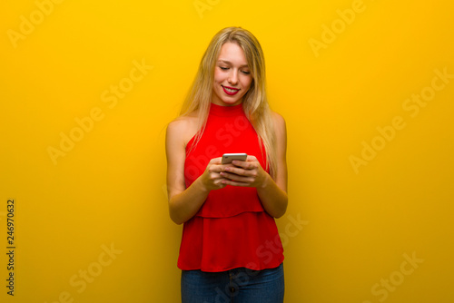 Young girl with red dress over yellow wall sending a message with the mobile