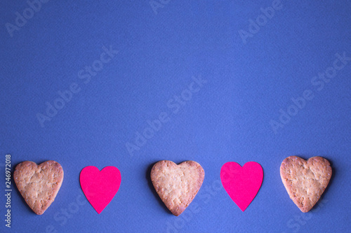 Heart-shaped gingerbread and paper hearts on blue-gray background. Top view