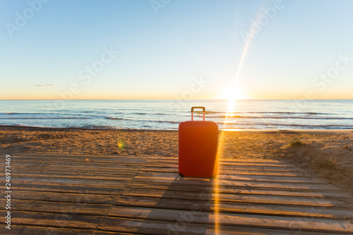 Luggage, holidays, travel concept - a red suitcase standing near the sea