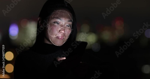 Asian Woman at night using facial recognition technology to unlock smart phone on street photo