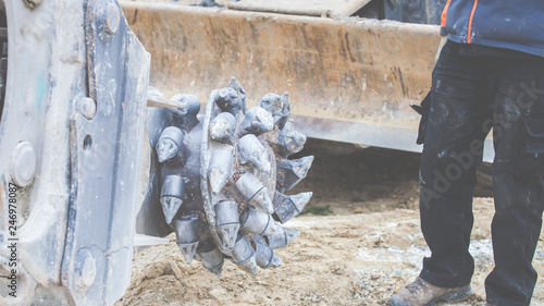 Ein Arbeiter steht neben dem Bohreraufsatz eines Baggers, mit dem Stein und Fels abgetragen werden kann.  