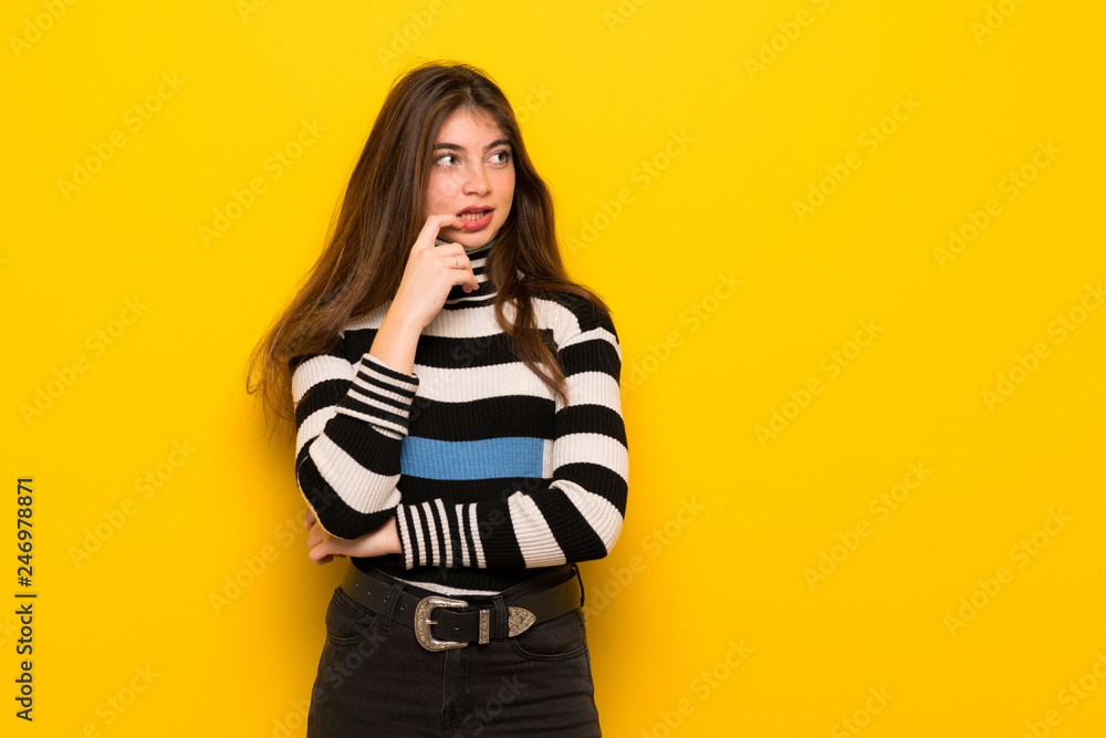 Young woman over yellow wall having doubts while looking up Young woman over yellow wall having doubts while looking up