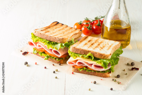 Close-up photo of a club sandwich. Sandwich with meat, prosciutto, salami, salad, vegetables, lettuce, tomato, onion and mustard on a fresh sliced rye bread on wooden background. Olives background.