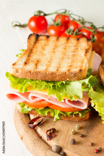 Close-up photo of a club sandwich. Sandwich with meat  prosciutto  salami  salad  vegetables  lettuce  tomato  onion and mustard on a fresh sliced rye bread on wooden background. Olives background.