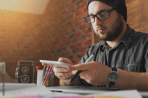 Young creative artist of web design in hat with graphic tablet in modern loft office
