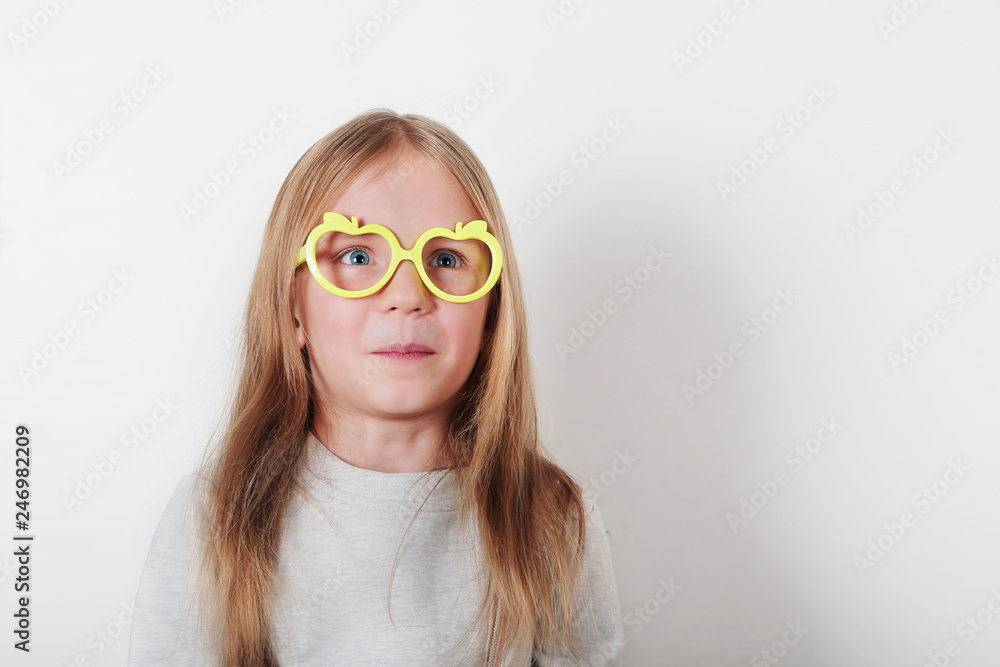 Portrait of happy surprised little girl in glasses making faces at camera, looking to the side. Expressive facial expressions . Human emotions, reactions, feelings and attitude . Portrait of happy surprised little girl in glasses making faces at camera, looking to the side. Expressive facial expressions . Human emotions, reactions, feelings and attitude .