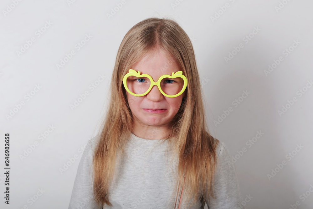  Portrait of naughty angry  little girl in glasses making faces at camera. Expressive facial expressions . Human emotions, reactions, feelings and attitude .