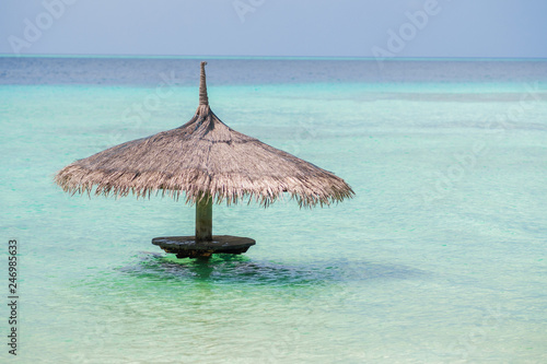Straw umbrella in the water, free space on the right. Resort on a tropical island