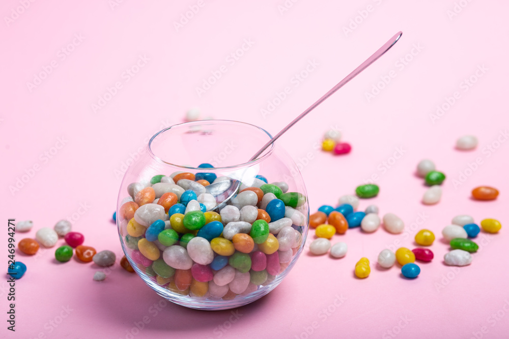colorful candy in clear wrappers piled in a glass vase isolated on pink background colorful candy in clear wrappers piled in a glass vase isolated on pink background