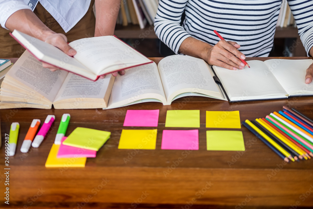 Young students classmates help friend catching up workbook and learning tutoring in a library, education and school concept Young students classmates help friend catching up workbook and learning tutoring in a library, education and school concept