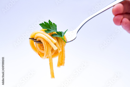 Spaghetti on a fork with fresh green parsley on white background. Homemade delicious pasta with tomato sauce