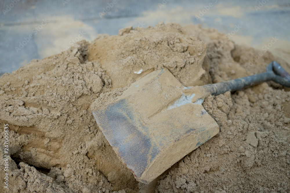 The spade stained with cement and concrete lies on a pile of sand. The spade stained with cement and concrete lies on a pile of sand.