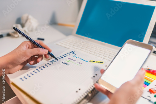 Woman hand writing in agenda consulting a mobile phone on a desk at home or office