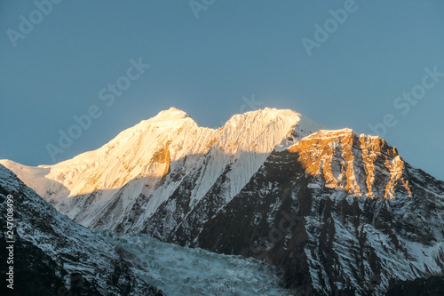 Annapurna III captured with the first sun rays on it's peak, during the sunrise. Seen from Chame, Annapurna Circuit Trek, Nepal. Clear sky above the peak. Valley still covered with shadows.