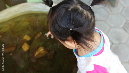 Asian little girl stand beside fish pond in the garden.It risky for children to Drown. kid in dangerous situation at home.Concept of dangerous in child.