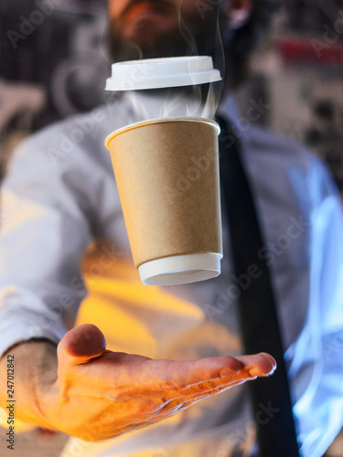 Levitating in the air paper cup with hot coffee. Barista, a bearded young man in a white shirt with a tie, creates miracles - advertises his drink, causing it to soar. Logoplacement concept photo