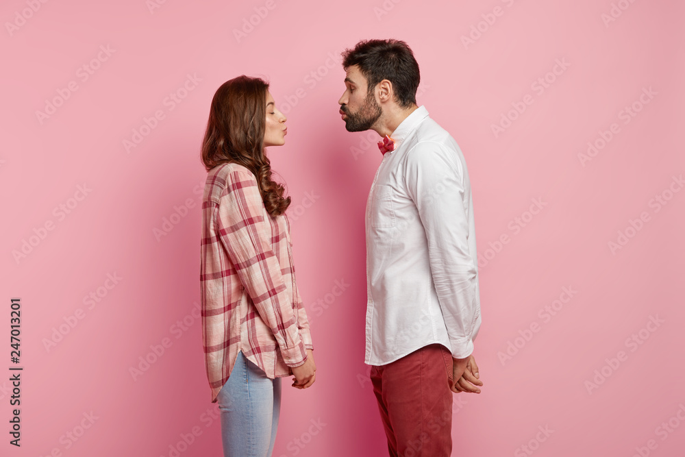 Shot of beautiful couple in love face each other, pout lips and going to kiss, close eyes from pleasure, dressed in stylish clothes, have date, isolated over pink background. Romantic relationships Shot of beautiful couple in love face each other, pout lips and going to kiss, close eyes from pleasure, dressed in stylish clothes, have date, isolated over pink background. Romantic relationships